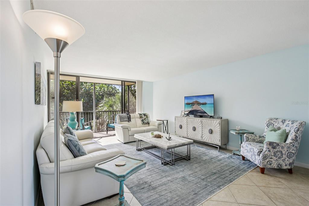 A living room features white leather sofas, a patterned armchair, and a balcony with greenery — 4900 OCEAN BOULEVARD UNIT 201, SARASOTA, FL
