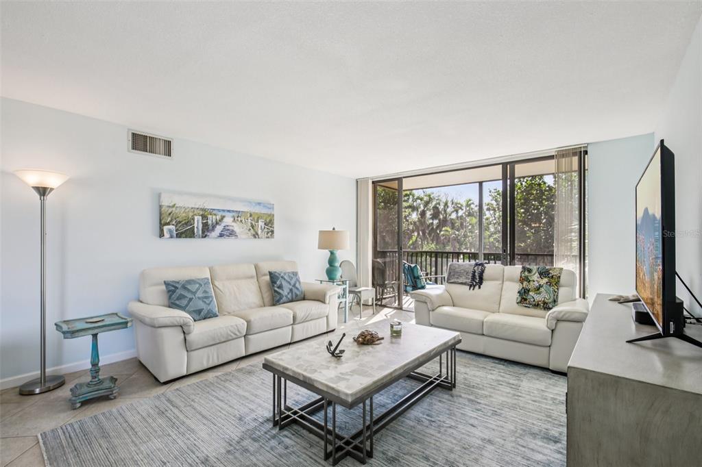 A living room features two white sofas, a stone coffee table, and a sliding glass door — 4900 OCEAN BOULEVARD UNIT 201, SARASOTA, FL