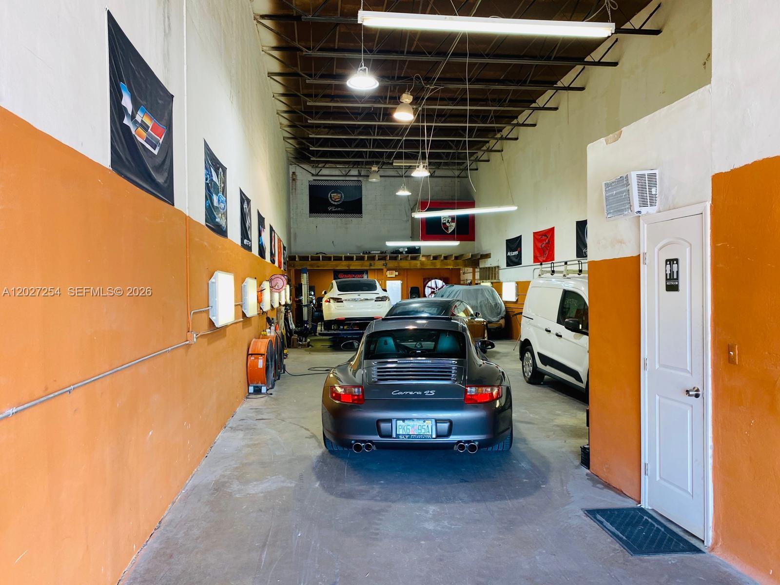 A garage interior features a gray Porsche, a white van, and orange-painted walls — HIALEAH, FL