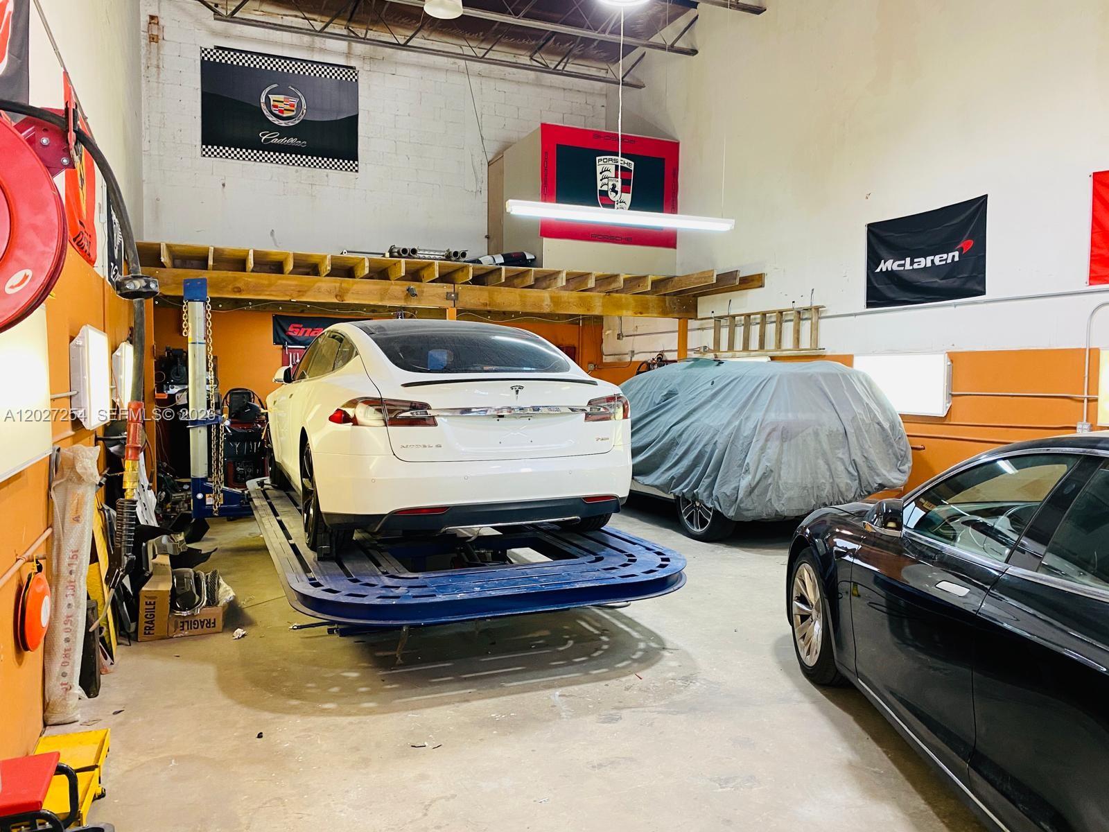 A garage workshop features a white Tesla on a lift and a car under a cover — HIALEAH, FL