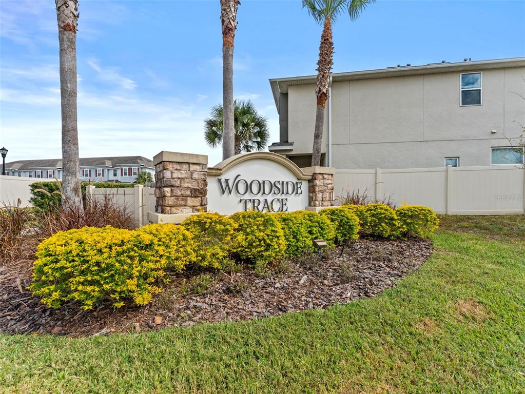 A stone monument sign for Woodside Trace stands in front of a tan building — 26399 LIMESTONE SPRINGS WAY, WESLEY CHAPEL, FL