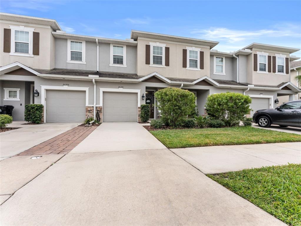 A row of two-story townhomes features beige stucco exteriors, attached garages, and concrete driveways — 26399 LIMESTONE SPRINGS WAY, WESLEY CHAPEL, FL