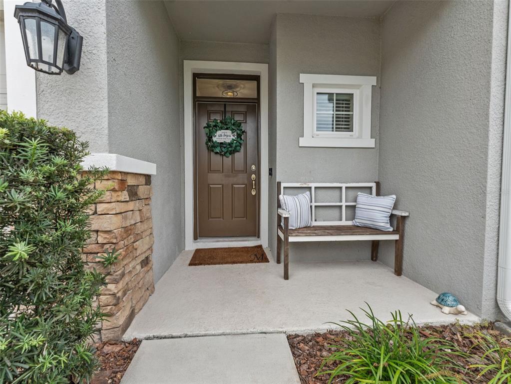 A front porch features a brown door, a wooden bench, and a stone-accented wall — 26399 LIMESTONE SPRINGS WAY, WESLEY CHAPEL, FL