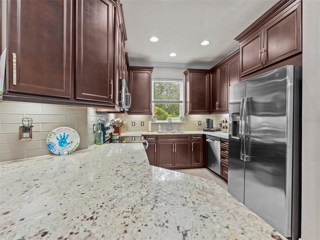 A kitchen features dark wood cabinets, granite countertops, stainless steel appliances, and a subway tile backsplash — 26399 LIMESTONE SPRINGS WAY, WESLEY CHAPEL, FL