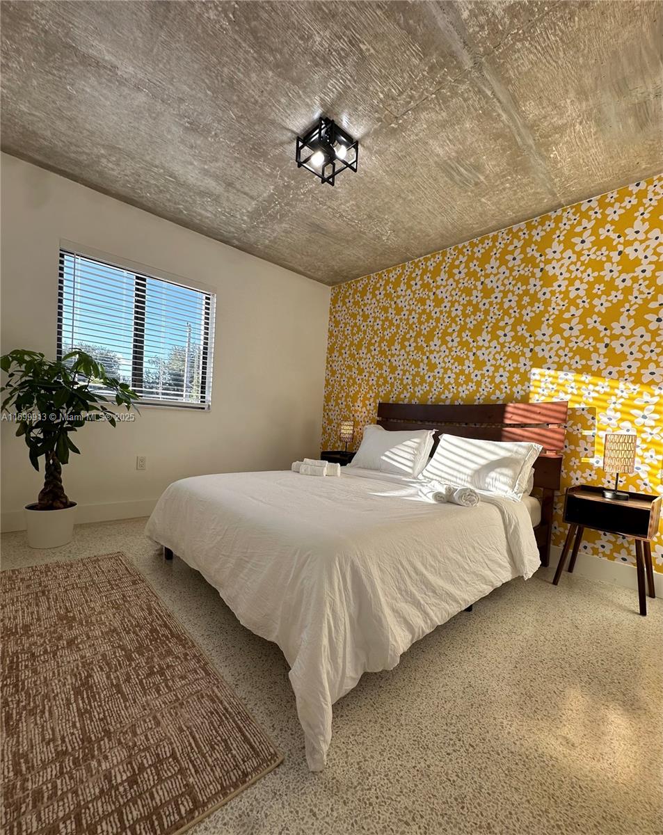 A bedroom features a bed against a yellow floral wallpaper wall and a concrete ceiling — 190 NW 69th St # 7, Miami FL 33150, MIAMI, FL