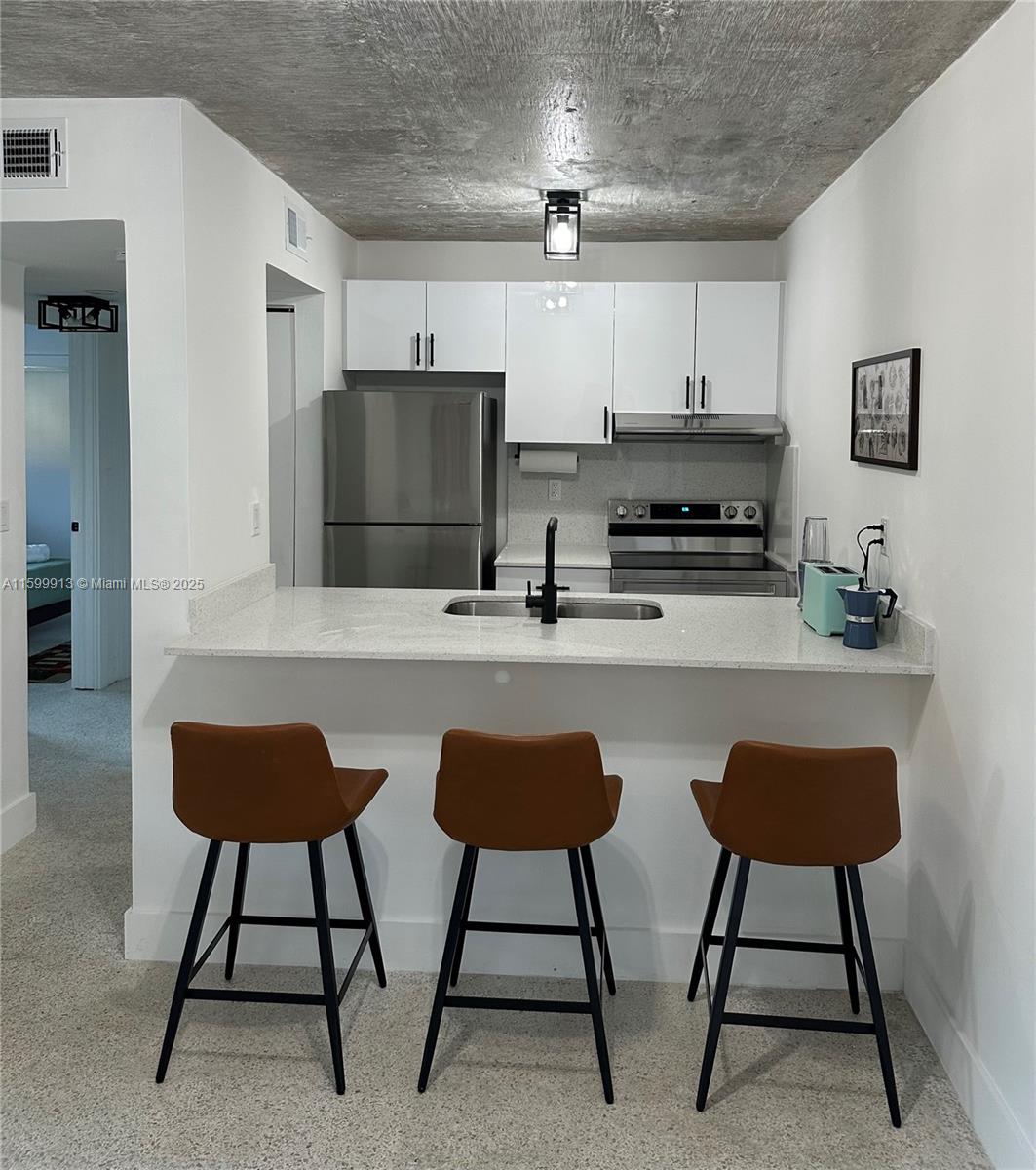 A kitchen features white cabinets, stainless steel appliances, a breakfast bar, and a concrete ceiling — 190 NW 69th St # 7, Miami FL 33150, MIAMI, FL