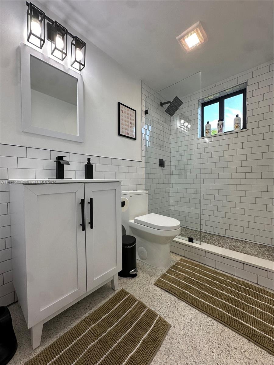 A modern bathroom features a white vanity, a glass-enclosed shower, and white subway tile walls — 190 NW 69th St # 7, Miami FL 33150, MIAMI, FL