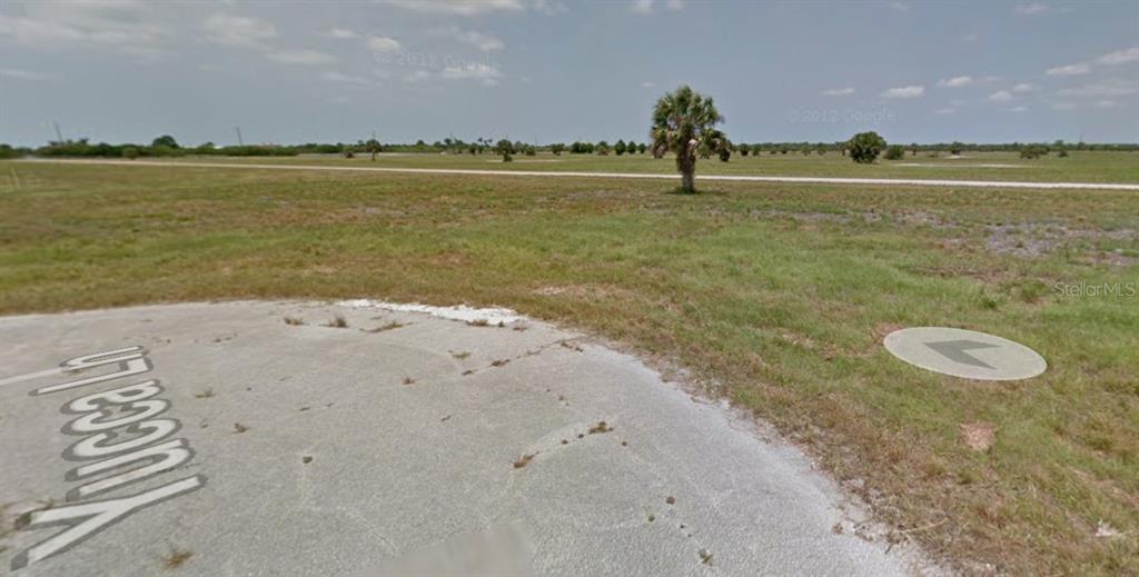 A paved road corner labeled Yucca Ln borders a large, flat, grassy vacant lot — 1 YUCCA LANE, PLACIDA, FL
