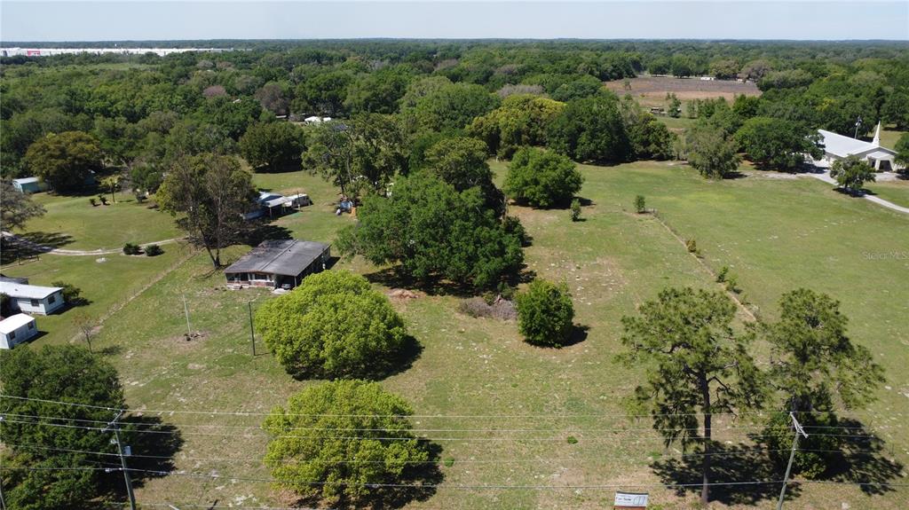 An aerial view shows a rural property with a house, trees, and open grassy fields — 31221 STATE ROAD 52, SAN ANTONIO, FL