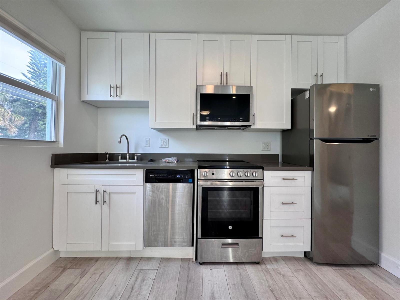 A kitchen features white cabinets, stainless steel appliances, a dark countertop, and light wood flooring — 102 S K Street Unit 4, FL 33460, FL