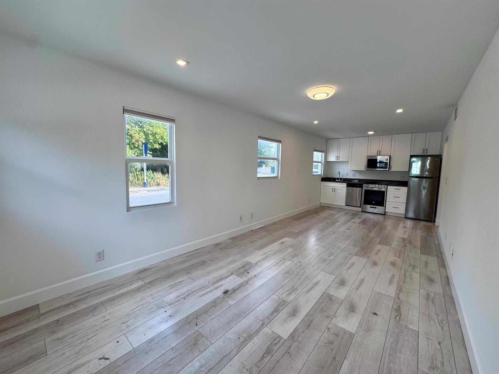 An open-concept kitchen and living area features white cabinets, stainless steel appliances, and wood-look flooring — 102 S K Street Unit 4, FL 33460, FL