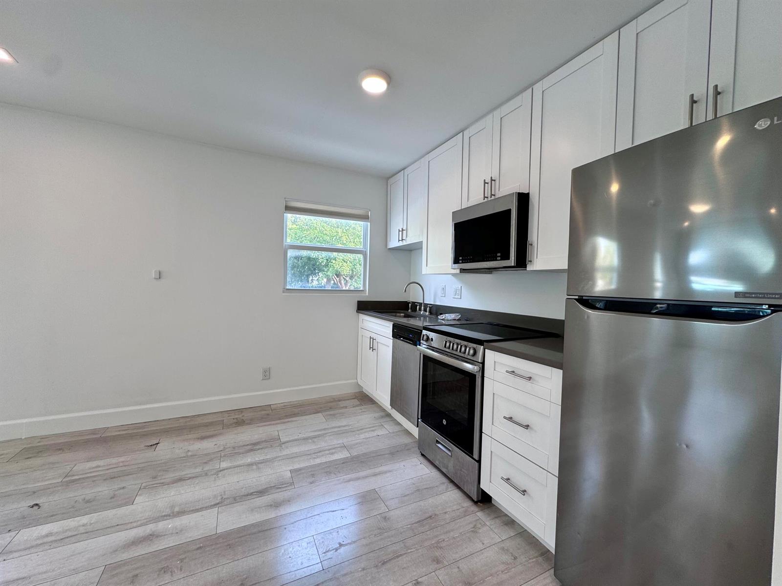 A kitchen features white cabinets, stainless steel appliances, dark countertops, and light wood-look flooring — 102 S K Street Unit 4, FL 33460, FL