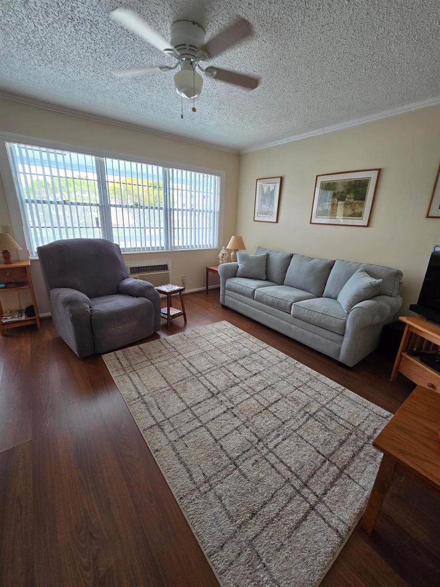 A living room features a grey sofa, a recliner, wood flooring, and a ceiling fan — 111 Lyndhurst E # 111, Deerfield Beach FL 33442, DEERFIELD BEACH, FL