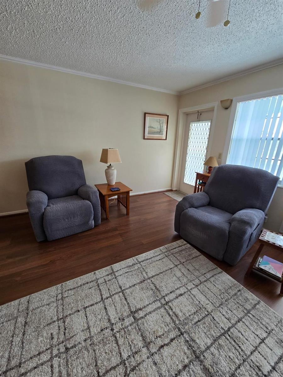 A living room features two gray recliners, a wooden side table, and a patterned rug — 111 Lyndhurst E # 111, Deerfield Beach FL 33442, DEERFIELD BEACH, FL