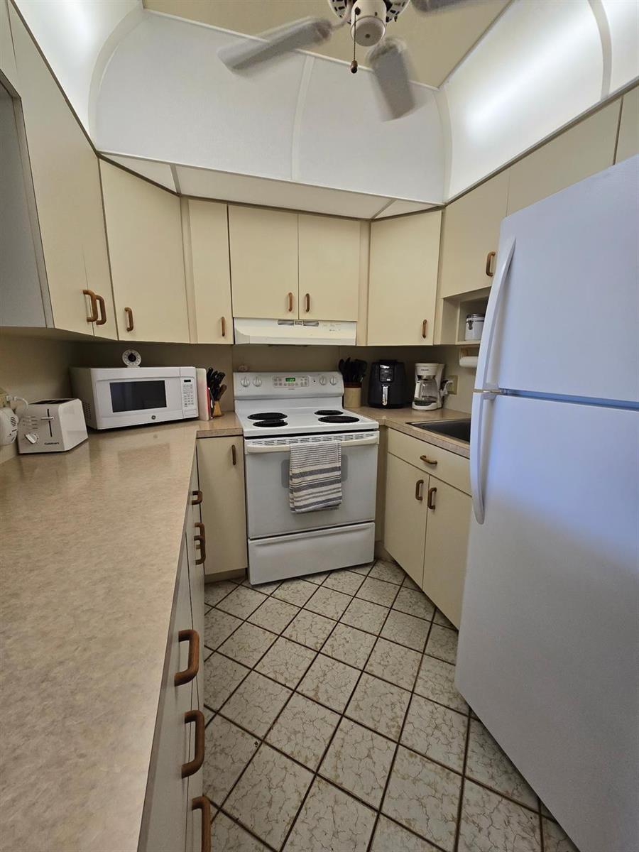 A kitchen features beige cabinets, white appliances, laminate countertops, and a tiled floor — 111 Lyndhurst E # 111, Deerfield Beach FL 33442, DEERFIELD BEACH, FL