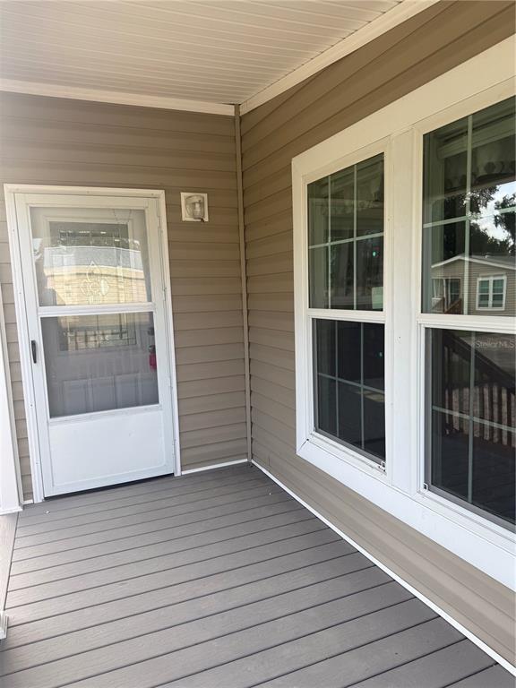A covered porch features gray composite decking, tan vinyl siding, a storm door, and windows — 10386 SE 52 COURT UNIT 12, BELLEVIEW, FL