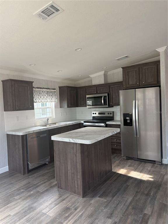 A kitchen features dark wood cabinets, a marble-look island, stainless steel appliances, and wood flooring — 10386 SE 52 COURT UNIT 12, BELLEVIEW, FL