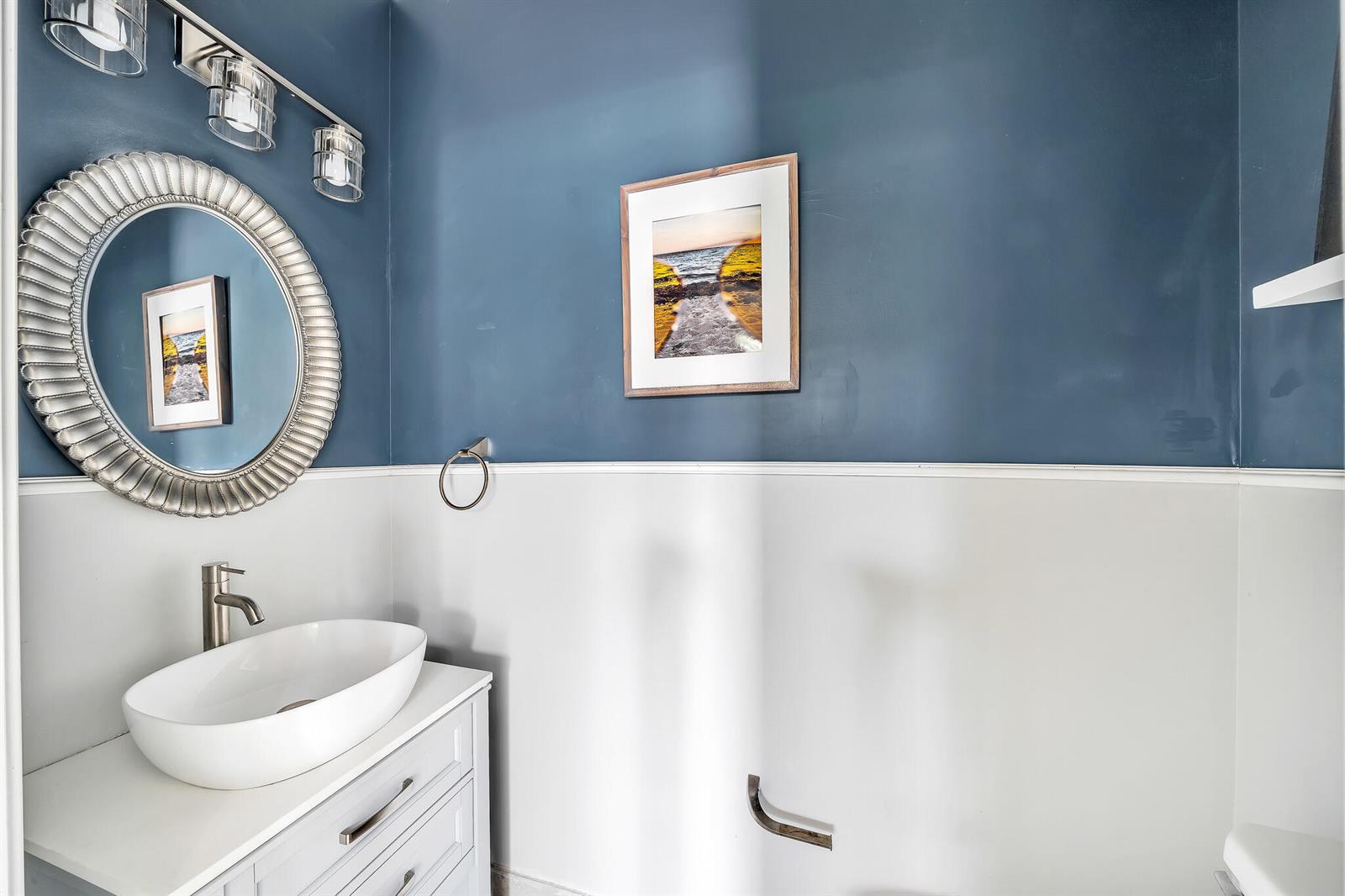 A bathroom features a white vanity, a round silver mirror, and blue and white walls — 4656 Silver Saw Lane, Lake Worth FL 33463, LAKE WORTH, FL