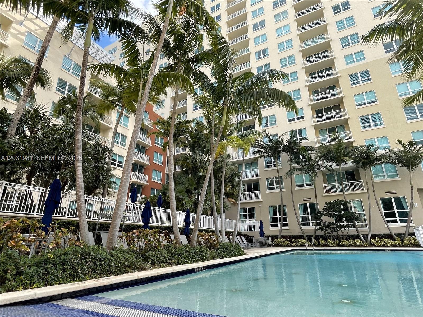 A swimming pool sits in front of a tall, multi-story apartment building with palm trees — 2000 N Bayshore Dr # 525, Miami FL 33137, MIAMI, FL