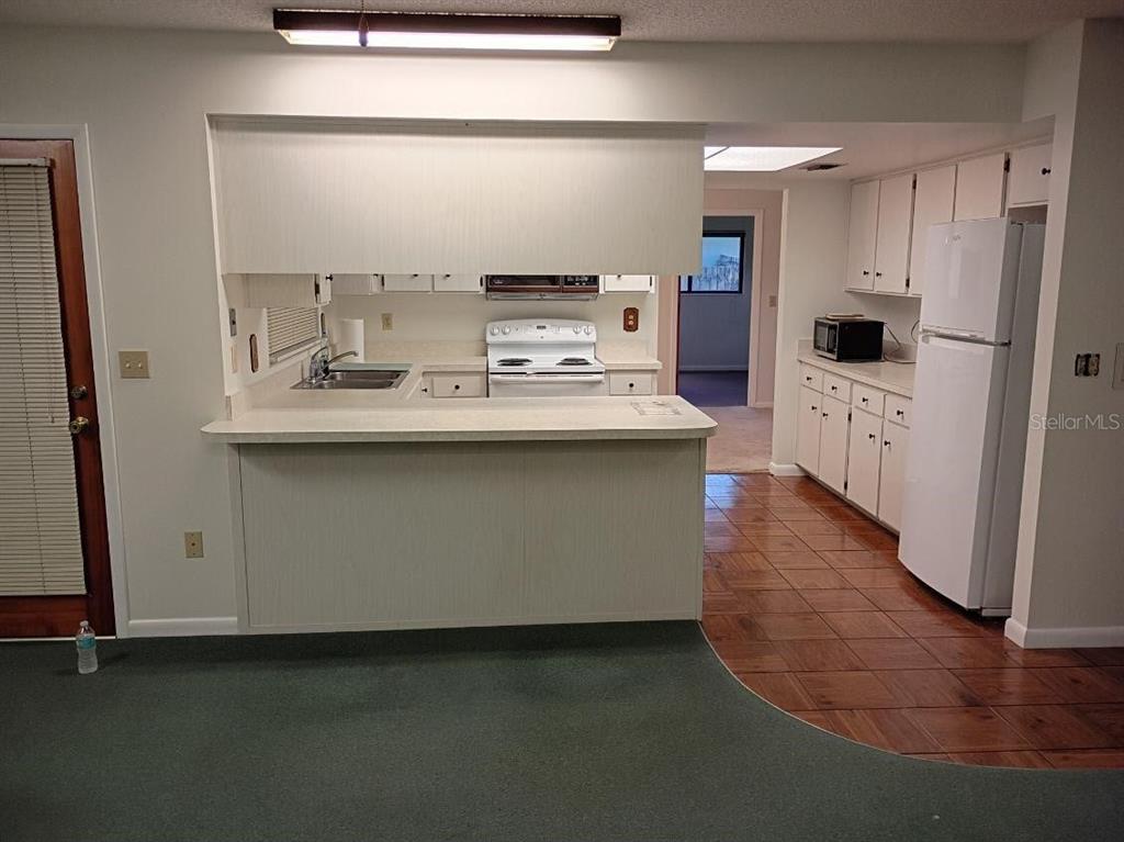 A kitchen features white cabinets, a breakfast bar, and tile flooring adjacent to carpeted space — 4145 POLARIS AVENUE, TITUSVILLE, FL