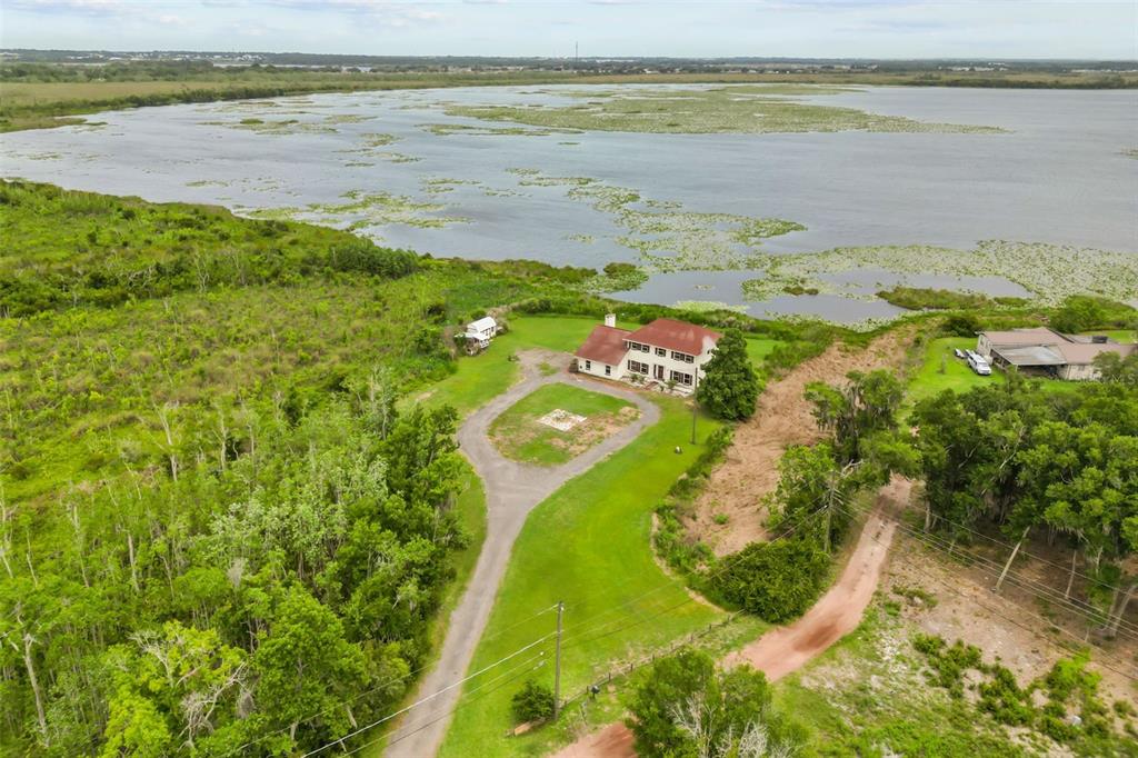 An aerial view shows a house with a red roof situated near a large lake — 3101 LAKE LOWERY ROAD, HAINES CITY, FL