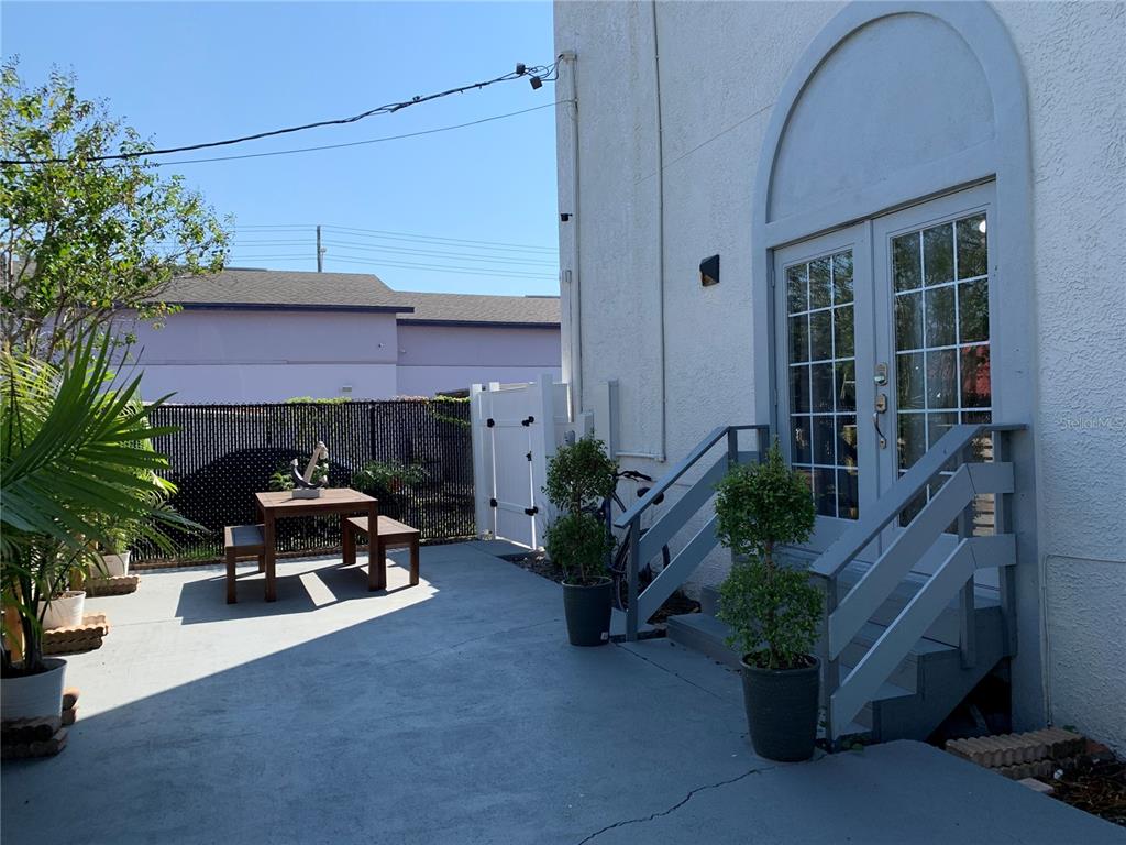 A concrete patio features a small wooden table, potted plants, and stairs leading to double doors — 1619 9TH AVENUE N, ST PETERSBURG, FL