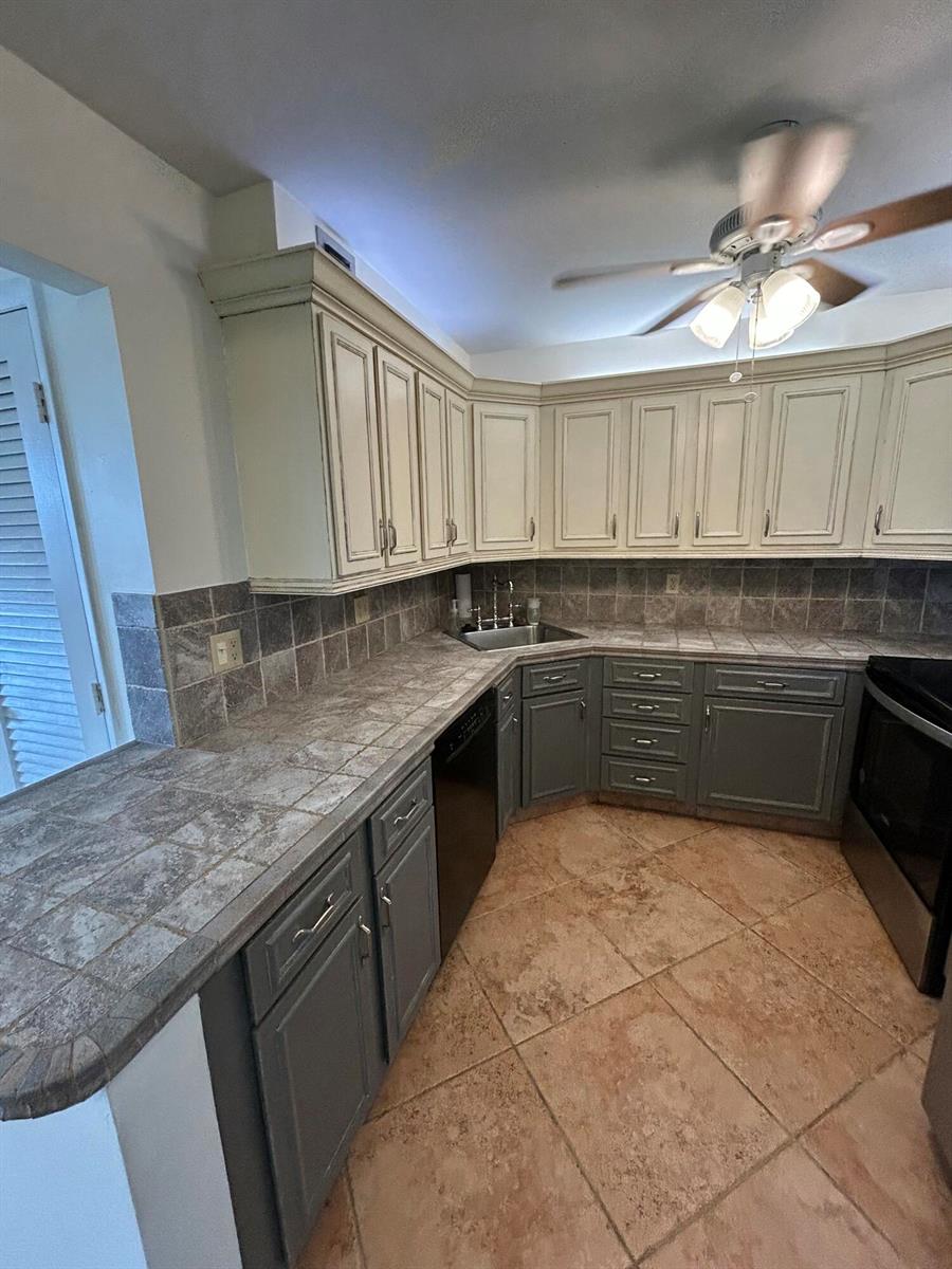 A kitchen features two-toned cabinets, tiled countertops, a corner sink, and light-colored floor tiles — 305 N Pompano Beach Boulevard # 205, Pompano Beach FL 33062, POMPANO BEACH, FL