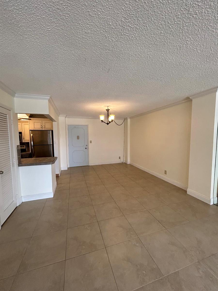 An open-concept dining area features beige tile flooring, a chandelier, and an adjacent kitchen — 305 N Pompano Beach Boulevard # 205, Pompano Beach FL 33062, POMPANO BEACH, FL