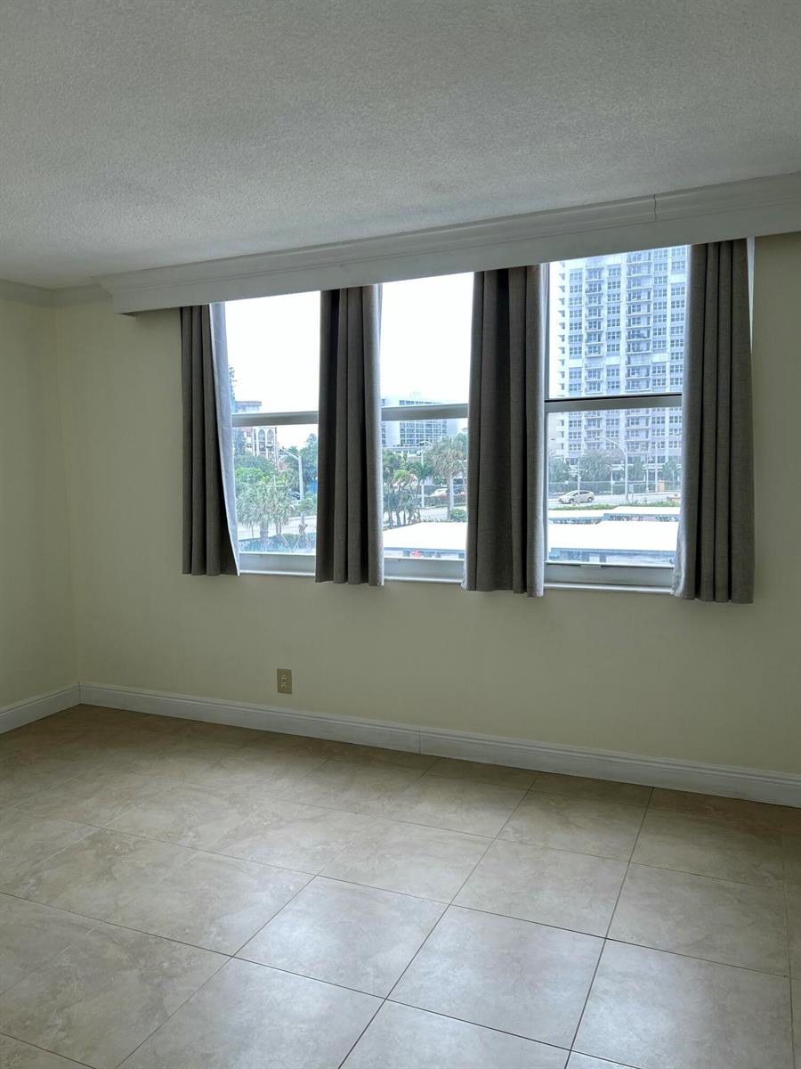 An empty room with light-colored tile flooring and three windows featuring gray curtains — 305 N Pompano Beach Boulevard # 205, Pompano Beach FL 33062, POMPANO BEACH, FL