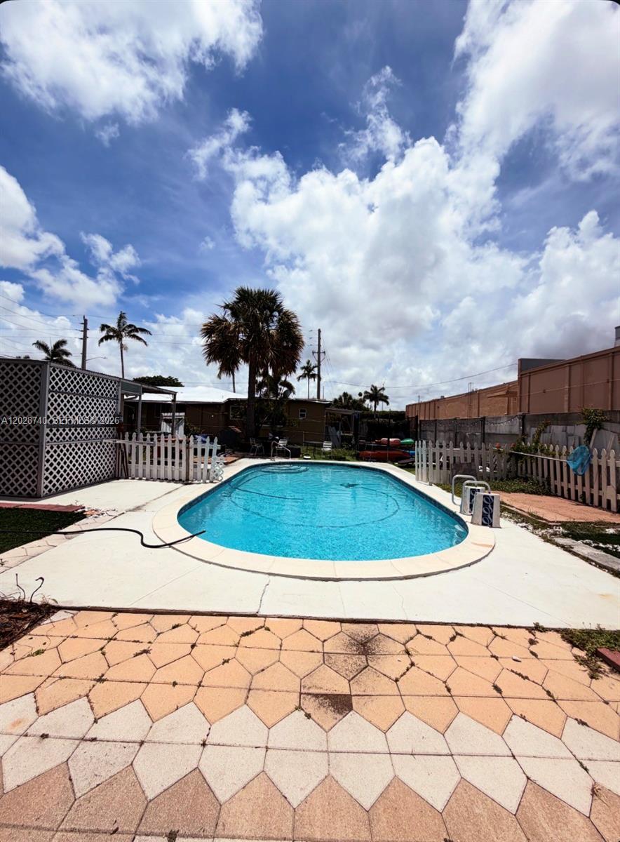 A backyard features an oval swimming pool surrounded by a paved patio and white fencing — 1077 SW 2nd St # 2, Hallandale Beach FL 33009, HALLANDALE BEACH, FL