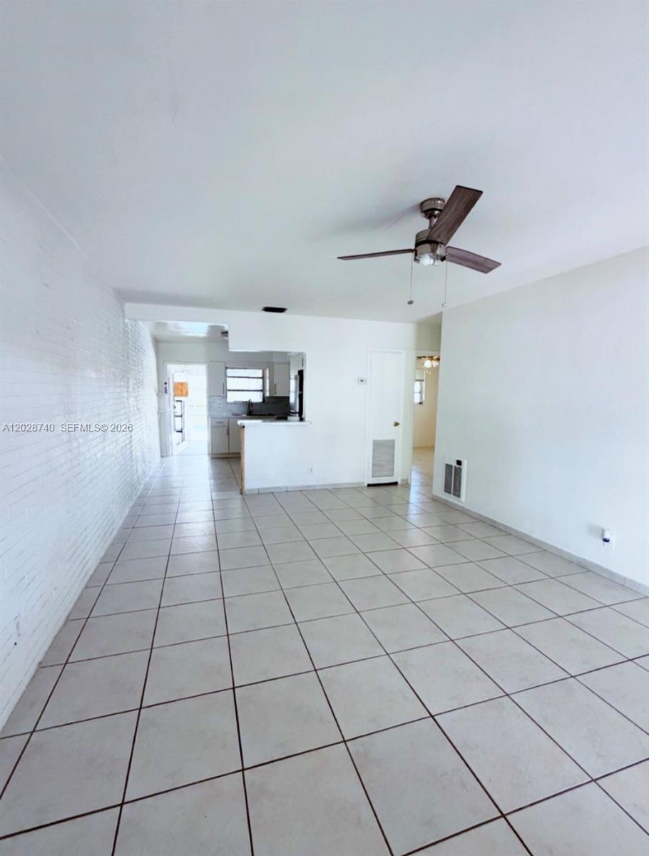 An open-concept living area features white tile flooring, a white brick wall, and a ceiling fan — 1077 SW 2nd St # 2, Hallandale Beach FL 33009, HALLANDALE BEACH, FL