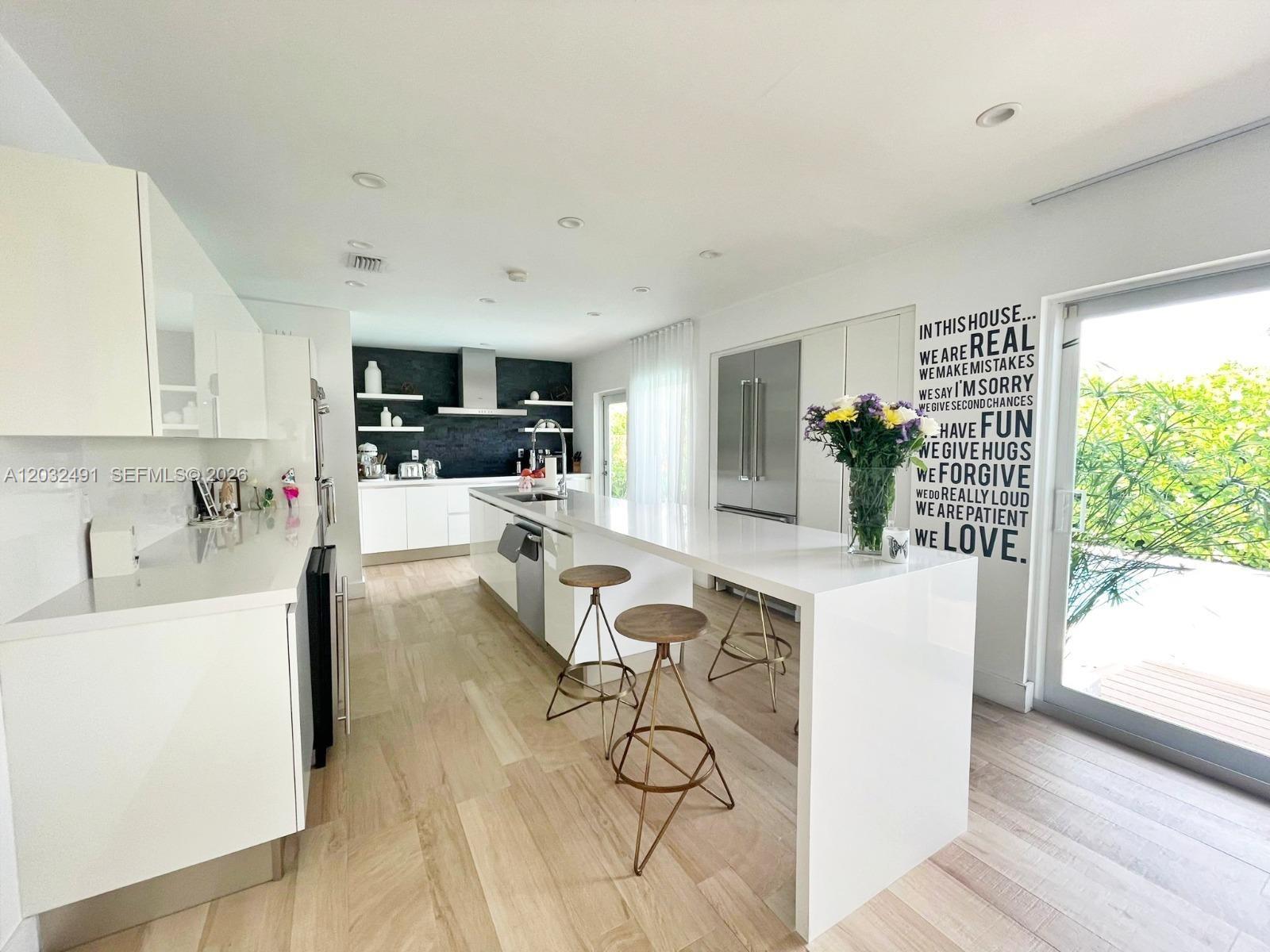 A modern white kitchen features a large island with bar stools and light wood flooring — 290 E Shore Dr E # 290, Miami FL 33133, MIAMI, FL