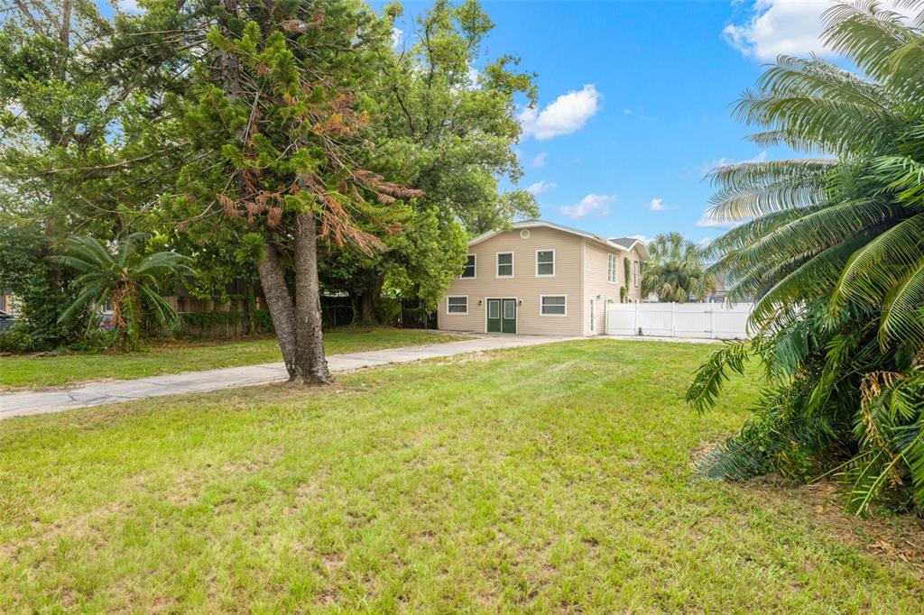 A two-story tan house with a concrete driveway sits on a grassy lot with trees — 305 E HANNA AVENUE, TAMPA, FL