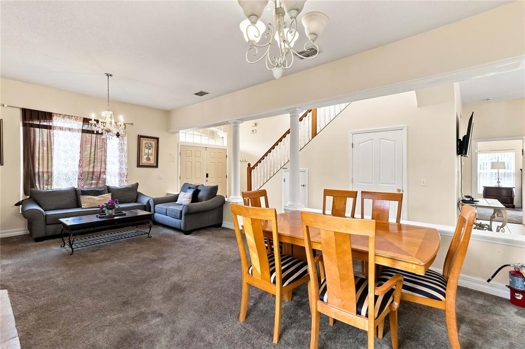 A living and dining area with carpeted floors, a staircase, and two chandeliers — 426 VISTA LOOP, DAVENPORT, FL