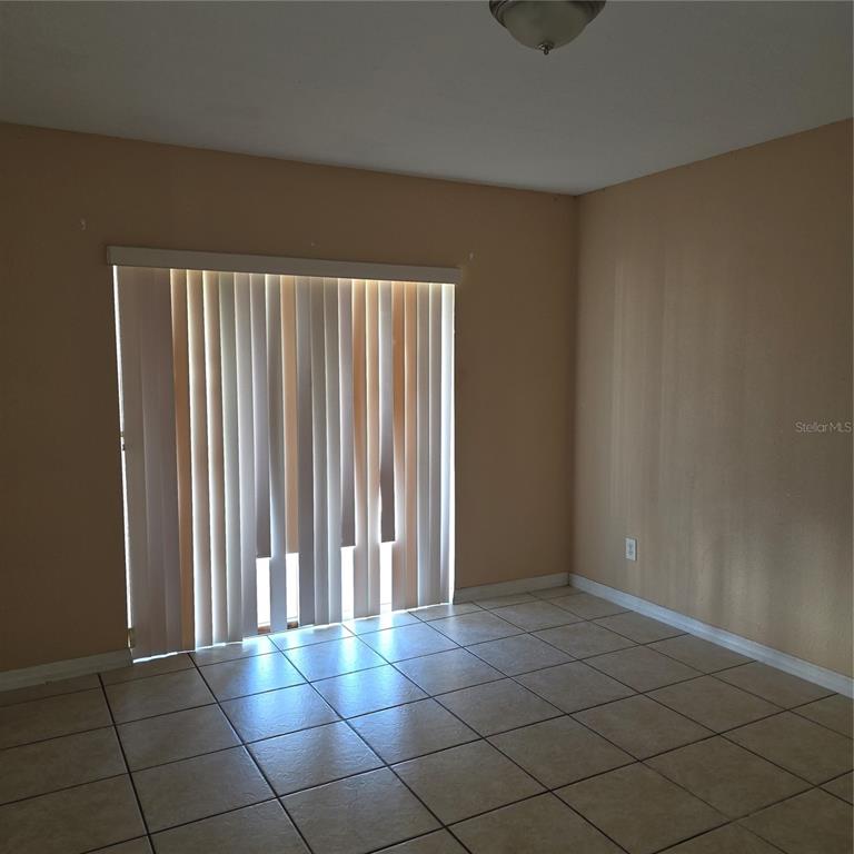 An empty room features beige walls, light-colored floor tiles, and a sliding glass door — 1707 MICHIGAN AVENUE UNIT D, KISSIMMEE, FL