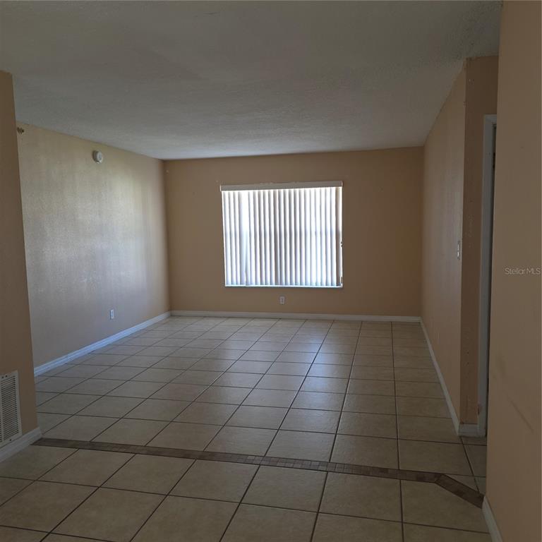 An empty room with beige walls, tile flooring, and a large window with vertical blinds — 1707 MICHIGAN AVENUE UNIT D, KISSIMMEE, FL