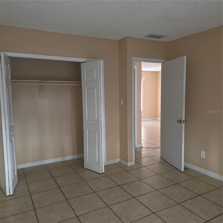 A room with beige walls, tiled flooring, an open closet, and an open doorway — 1707 MICHIGAN AVENUE UNIT D, KISSIMMEE, FL