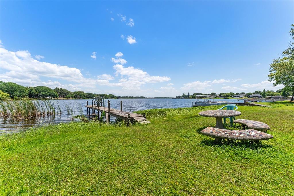 A grassy lakeshore features a wooden dock, a stone picnic table, and a pontoon boat — 7570 BERKLEY ROAD, POLK CITY, FL