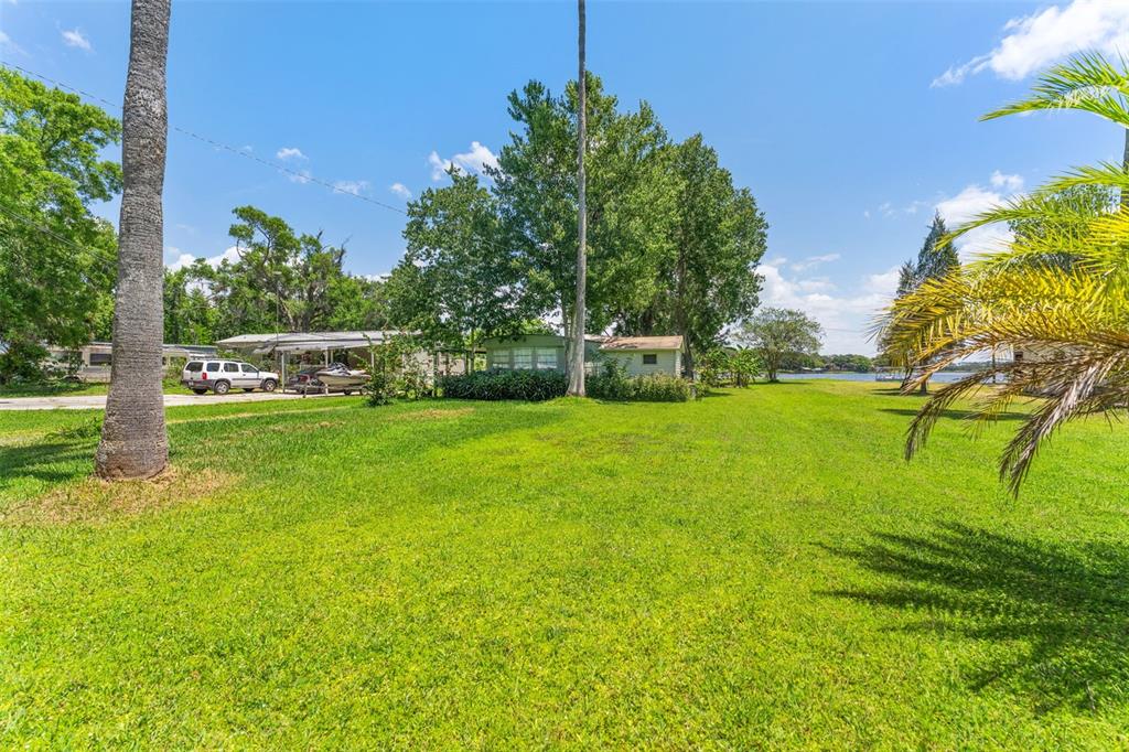 A grassy yard leads to a mobile home with a carport and nearby waterfront views — 7570 BERKLEY ROAD, POLK CITY, FL