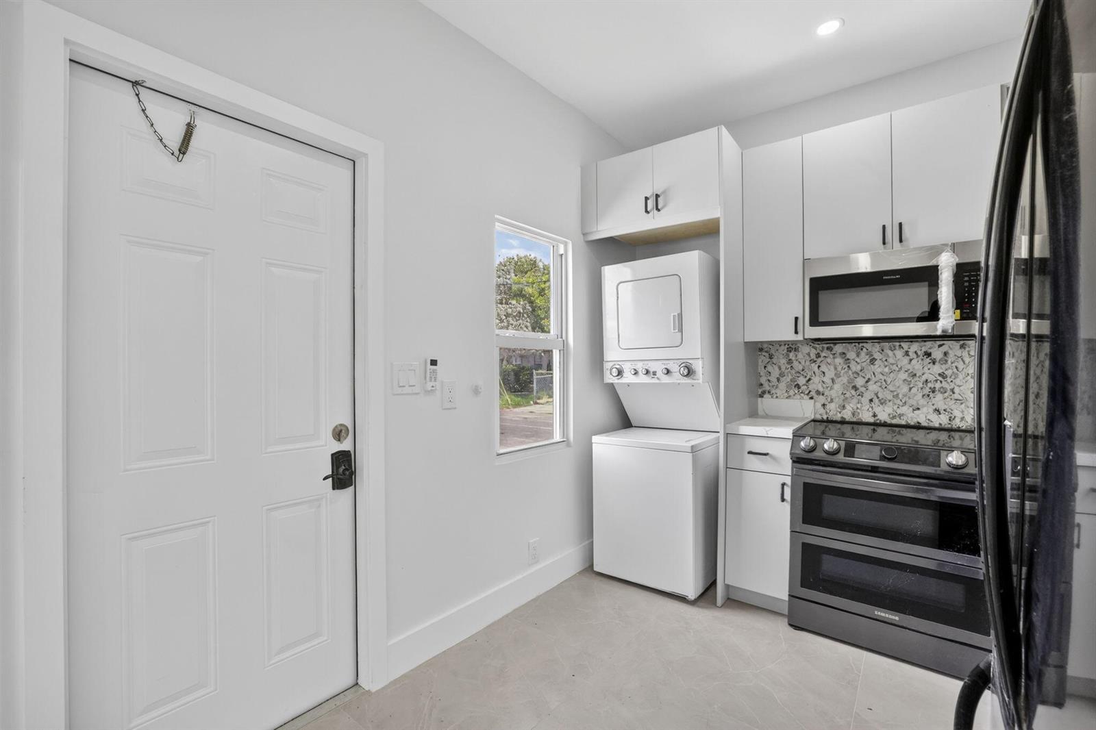 A kitchen area features a stacked washer-dryer, white cabinetry, and a black range — 621 NW 3rd Avenue, Pompano Beach FL 33060, POMPANO BEACH, FL