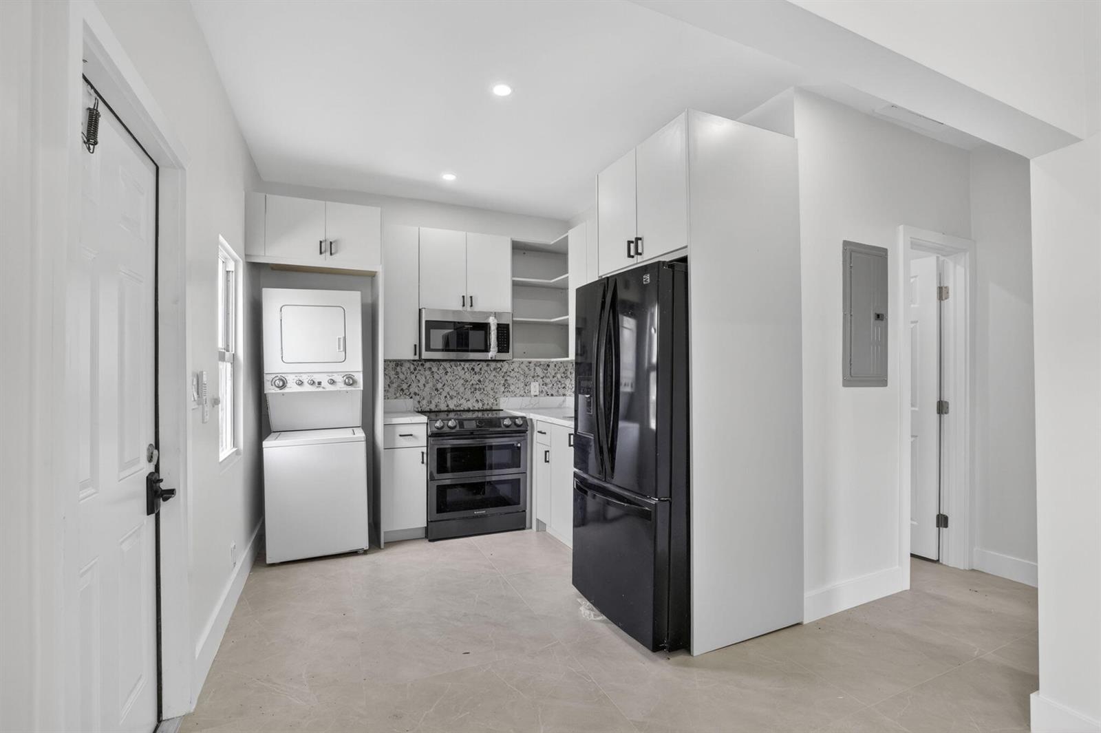 A kitchen features white cabinets, black appliances, a stacked washer-dryer unit, and light tile flooring — 621 NW 3rd Avenue, Pompano Beach FL 33060, POMPANO BEACH, FL