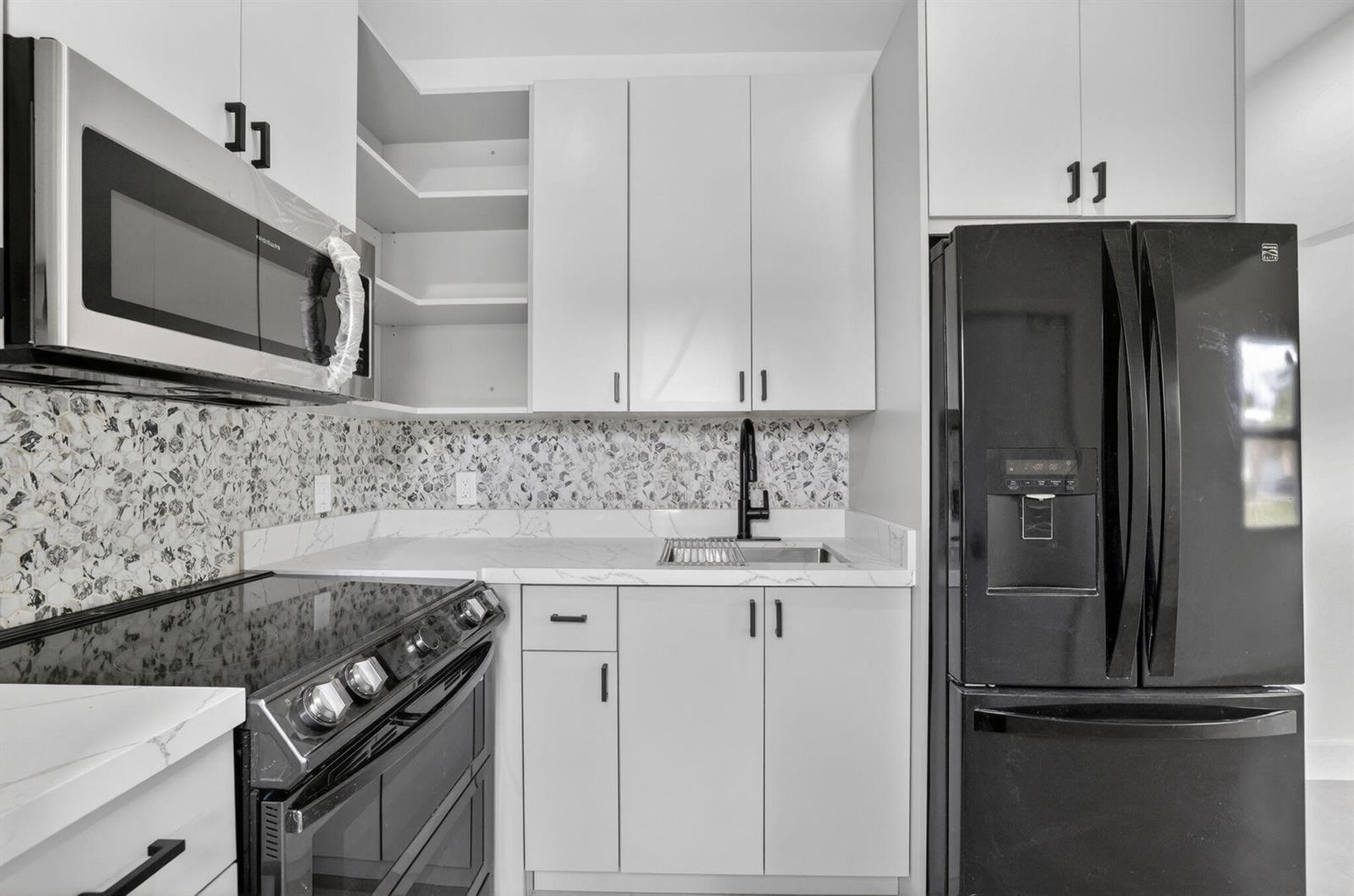 A kitchen features white cabinets, a black refrigerator, a microwave, and a patterned backsplash — 621 NW 3rd Avenue, Pompano Beach FL 33060, POMPANO BEACH, FL