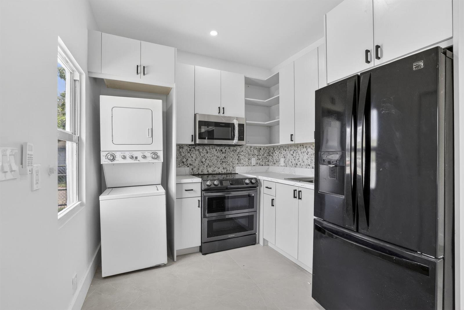 A kitchen features white cabinets, black appliances, a stacked washer-dryer unit, and patterned backsplash tile — 621 NW 3rd Avenue, Pompano Beach FL 33060, POMPANO BEACH, FL