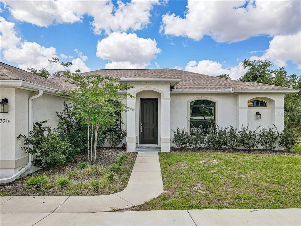 A single-story house with a white stucco exterior, arched entryway, and a dark front door — 7314 MADRID ROAD, WEEKI WACHEE, FL