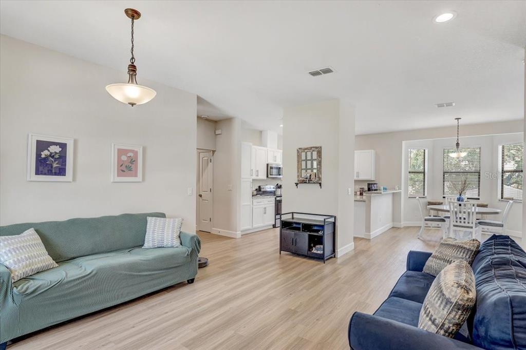 A living room with light wood flooring, two sofas, and an open-concept kitchen and dining area — 7314 MADRID ROAD, WEEKI WACHEE, FL