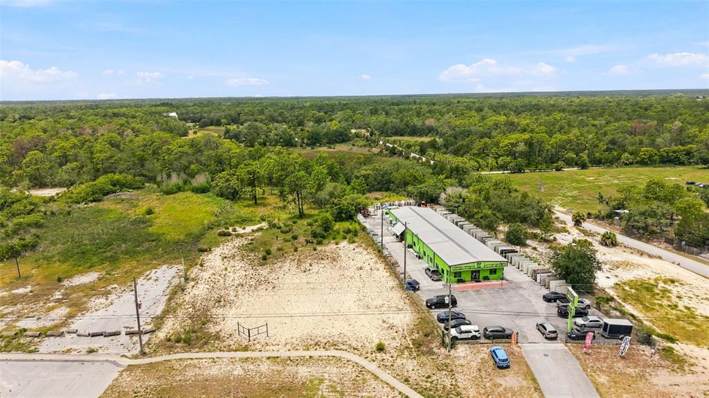 An aerial view shows a long, green commercial building surrounded by parking and undeveloped land — COMMERCIAL WAY, WEEKI WACHEE, FL