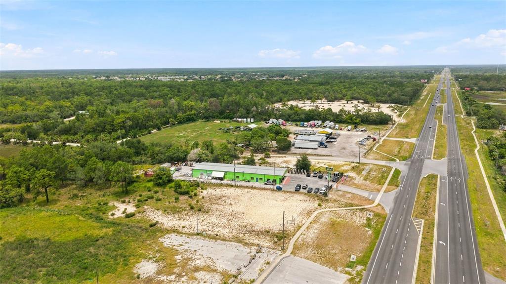 An aerial view shows a green commercial building situated next to a highway and forest — COMMERCIAL WAY, WEEKI WACHEE, FL