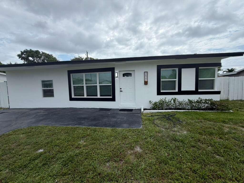 A white single-story house features black window trim, a black roofline, and a paved driveway — 2620 NE 7th Terrace, Pompano Beach FL 33064, POMPANO BEACH, FL