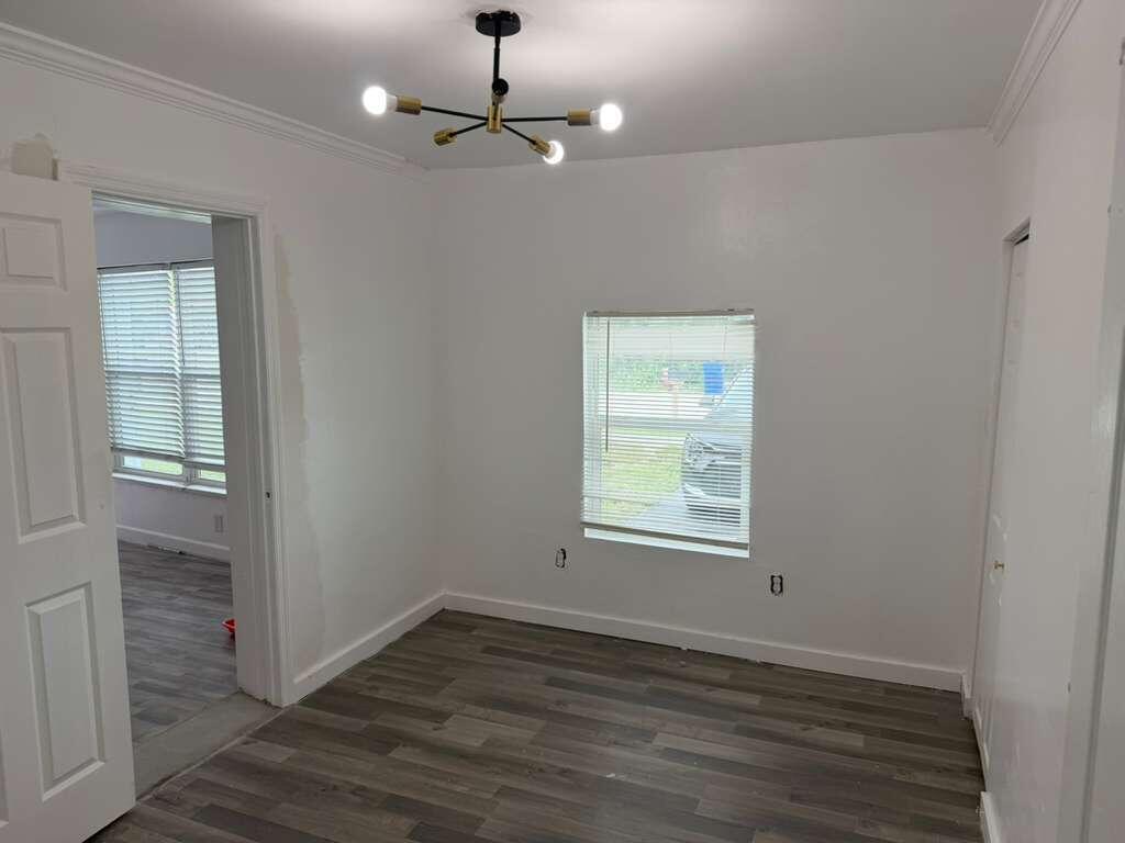 An empty room with white walls, gray wood-look flooring, a modern chandelier, and one window — 2620 NE 7th Terrace, Pompano Beach FL 33064, POMPANO BEACH, FL