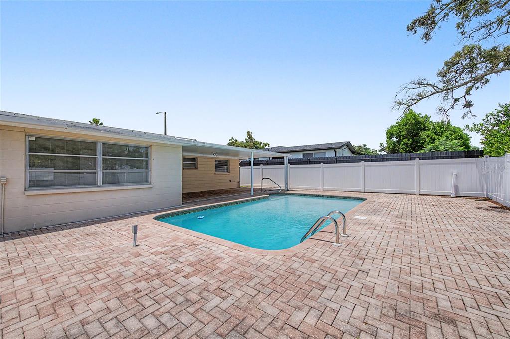 A backyard features a rectangular swimming pool surrounded by a brick paver patio and fence — 9830 RAINBOW LANE, PORT RICHEY, FL